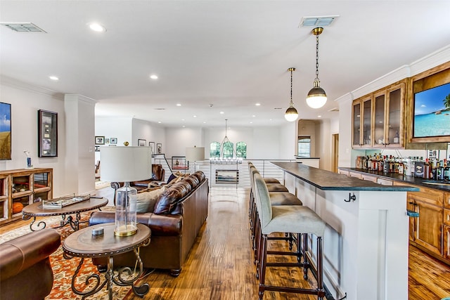 kitchen with hanging light fixtures, ornamental molding, a kitchen breakfast bar, and light hardwood / wood-style flooring