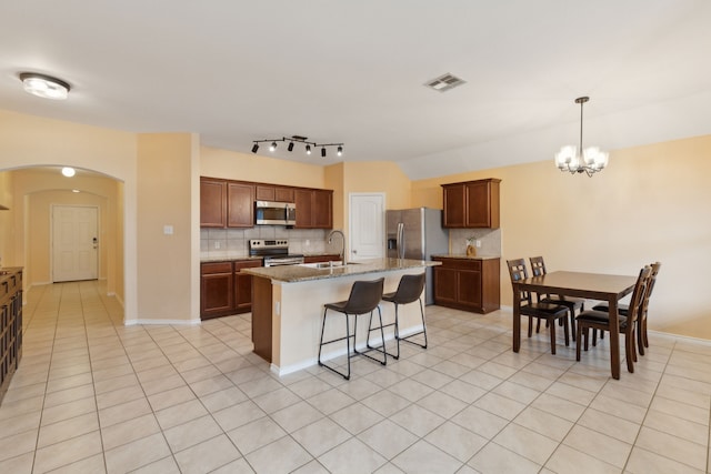 kitchen featuring a kitchen island with sink, light tile patterned floors, decorative light fixtures, and appliances with stainless steel finishes