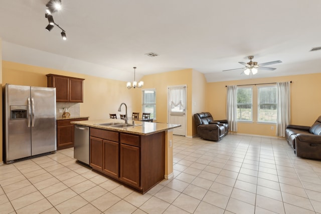 kitchen with sink, decorative light fixtures, appliances with stainless steel finishes, light stone countertops, and a kitchen island with sink