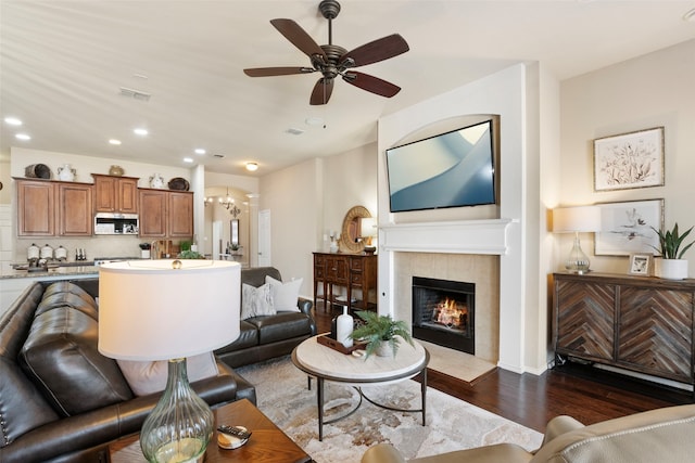 living room featuring dark hardwood / wood-style flooring, a tiled fireplace, and ceiling fan with notable chandelier