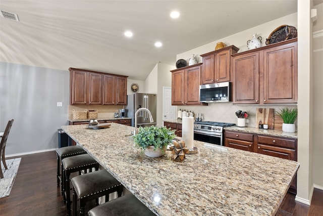 kitchen featuring light stone counters, backsplash, a large island with sink, and appliances with stainless steel finishes