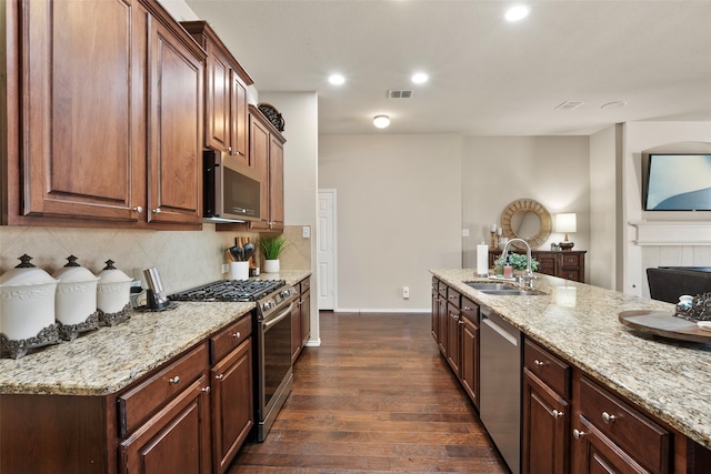 kitchen with sink, appliances with stainless steel finishes, dark hardwood / wood-style floors, light stone countertops, and decorative backsplash