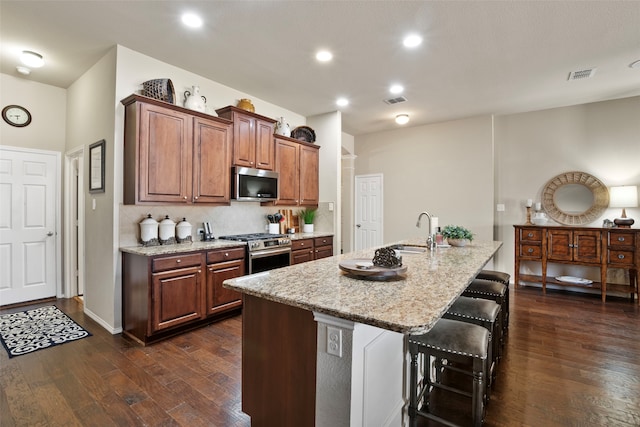 kitchen with appliances with stainless steel finishes, dark hardwood / wood-style floors, an island with sink, sink, and a breakfast bar area