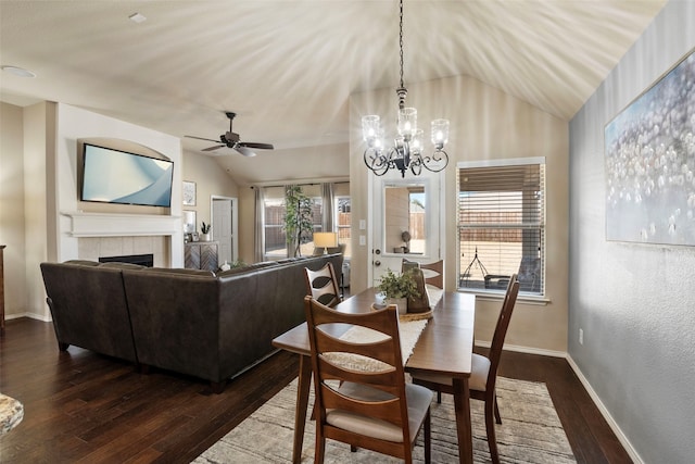 dining room with a tiled fireplace, a healthy amount of sunlight, lofted ceiling, and dark hardwood / wood-style floors