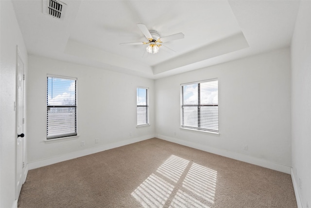 carpeted empty room featuring ceiling fan, plenty of natural light, and a raised ceiling