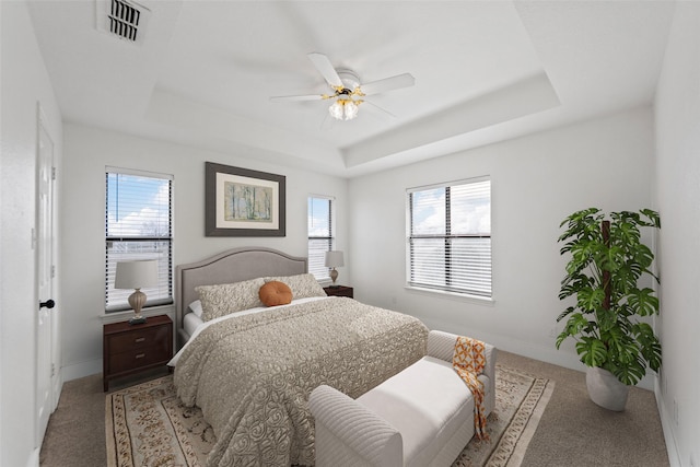 bedroom with ceiling fan, a raised ceiling, and multiple windows