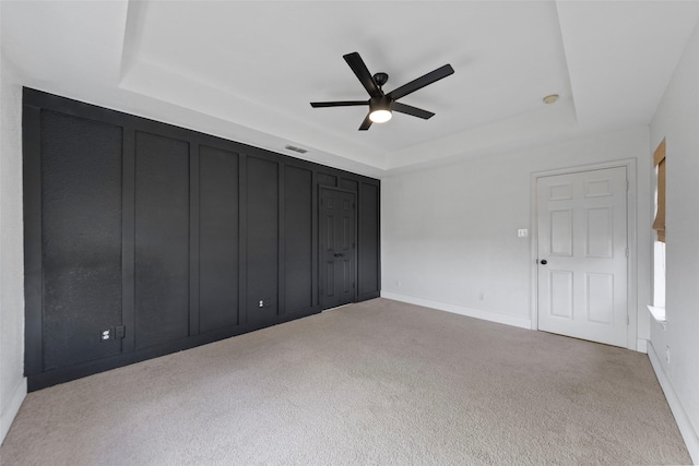 unfurnished bedroom with a raised ceiling, light carpet, and ceiling fan