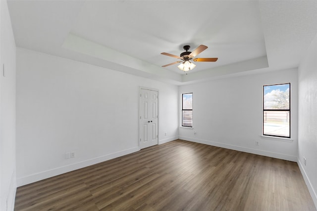 unfurnished room with a raised ceiling, ceiling fan, and dark hardwood / wood-style flooring