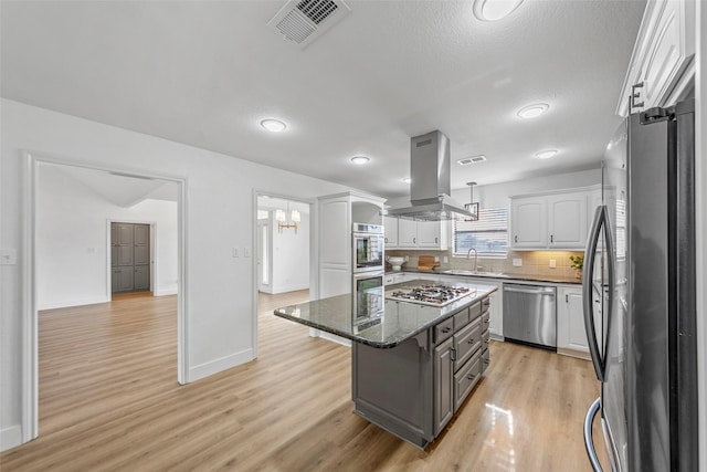 kitchen featuring appliances with stainless steel finishes, dark stone countertops, white cabinets, island exhaust hood, and a center island