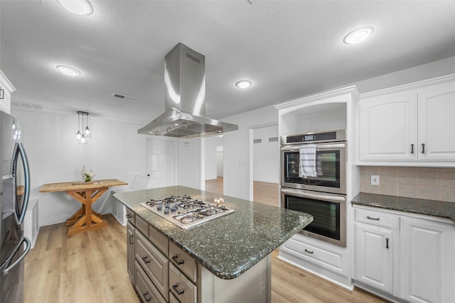 kitchen with appliances with stainless steel finishes, dark stone countertops, white cabinets, island exhaust hood, and a center island