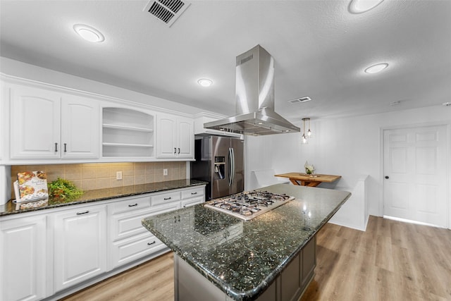 kitchen with island range hood, dark stone counters, white cabinets, and appliances with stainless steel finishes