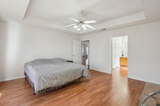 bedroom with ceiling fan, a tray ceiling, and hardwood / wood-style floors