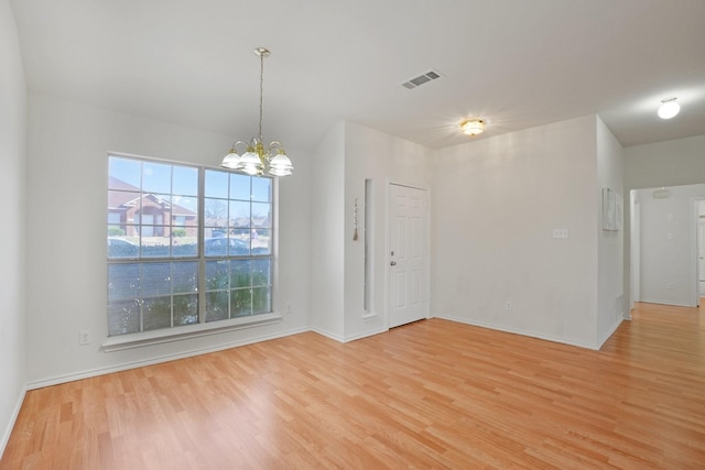 spare room with an inviting chandelier and light wood-type flooring