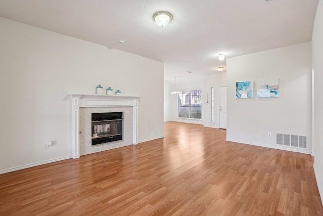 unfurnished living room with a tiled fireplace and light hardwood / wood-style flooring