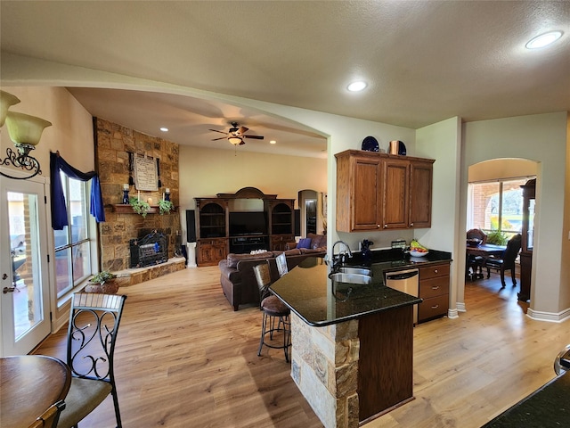 kitchen with a stone fireplace, sink, light wood-type flooring, and kitchen peninsula