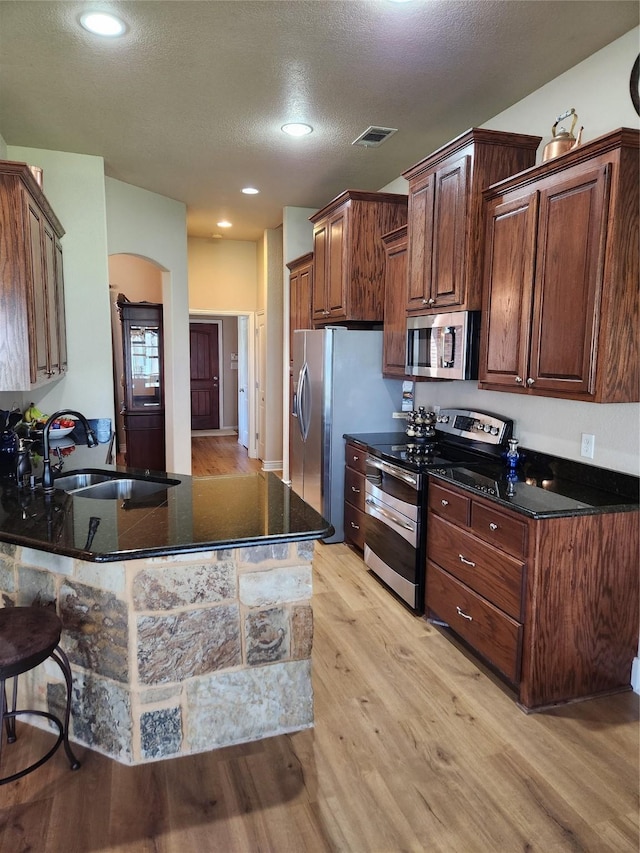 kitchen with sink, light hardwood / wood-style flooring, dark stone countertops, stainless steel appliances, and kitchen peninsula