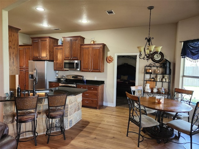 kitchen featuring pendant lighting, sink, appliances with stainless steel finishes, a notable chandelier, and light wood-type flooring