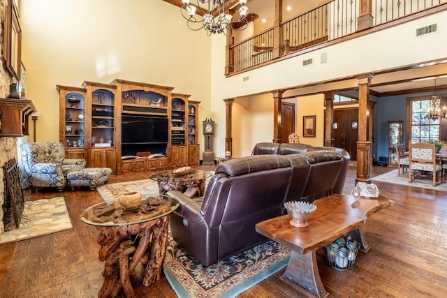 living room with ornate columns, wood-type flooring, a towering ceiling, and an inviting chandelier