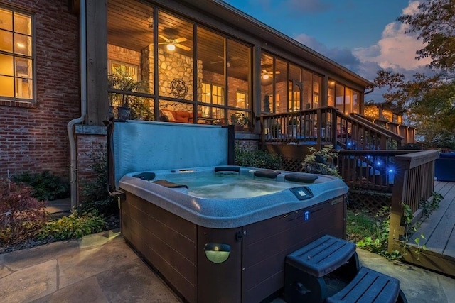 patio terrace at dusk featuring a hot tub and a wooden deck