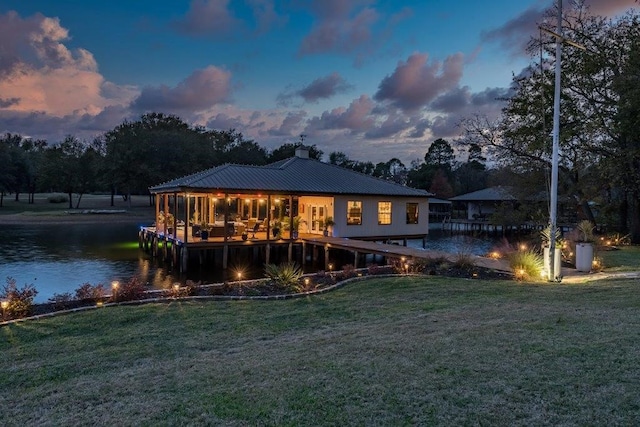 back house at dusk with a water view and a lawn