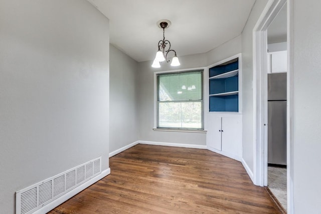 unfurnished room with an inviting chandelier and dark wood-type flooring