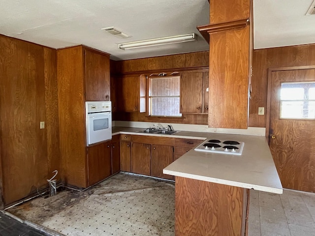 kitchen featuring sink, white appliances, kitchen peninsula, and wood walls