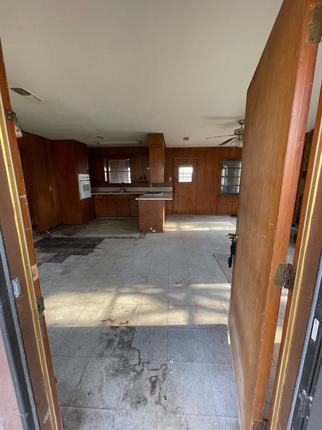 kitchen with white oven, sink, ceiling fan, and wood walls