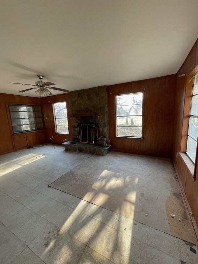 unfurnished living room featuring a stone fireplace and wood walls