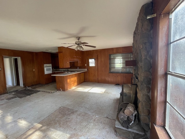 kitchen with ceiling fan, wooden walls, kitchen peninsula, and oven