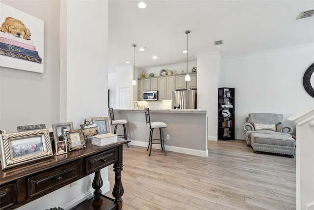 interior space with appliances with stainless steel finishes, backsplash, a kitchen bar, hanging light fixtures, and light hardwood / wood-style floors