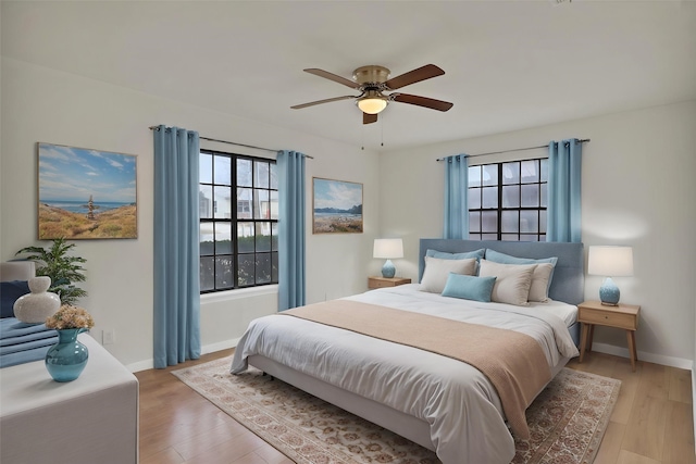 bedroom featuring multiple windows, baseboards, light wood-type flooring, and a ceiling fan