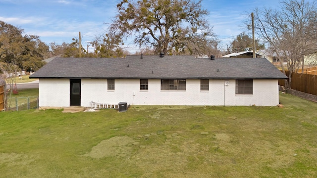 back of house featuring brick siding, fence, a lawn, and roof with shingles