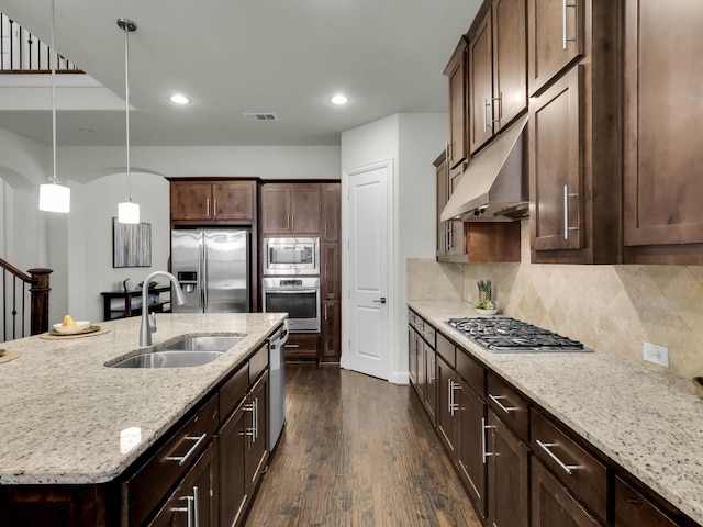 kitchen with light stone counters, sink, stainless steel appliances, and a center island with sink