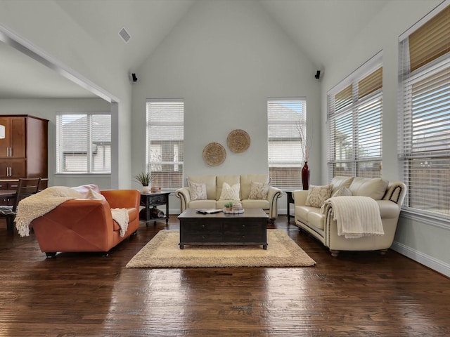 living room with a healthy amount of sunlight, dark hardwood / wood-style flooring, and high vaulted ceiling