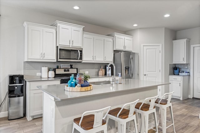 kitchen featuring sink, a breakfast bar, appliances with stainless steel finishes, an island with sink, and white cabinets