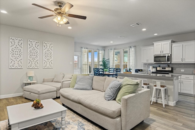 living room with ceiling fan, sink, and light wood-type flooring