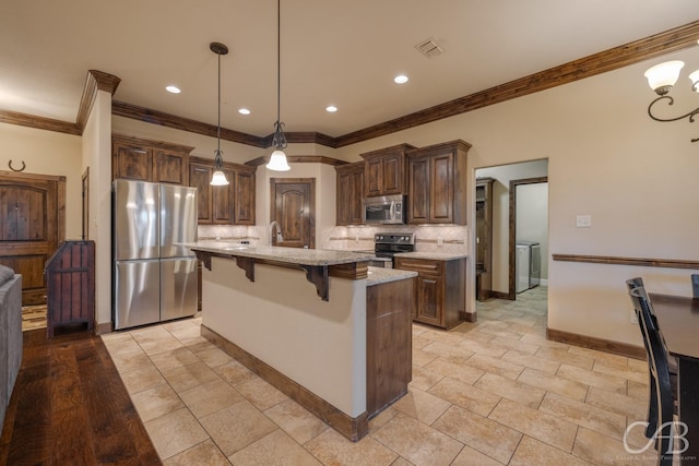 kitchen with a breakfast bar, appliances with stainless steel finishes, light stone countertops, an island with sink, and decorative light fixtures