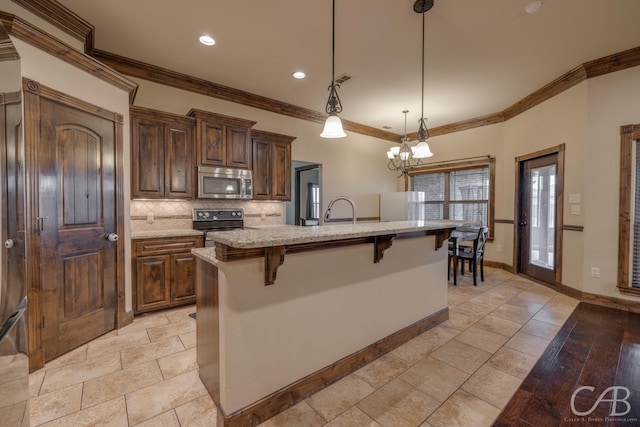 kitchen featuring a breakfast bar, pendant lighting, light stone counters, stainless steel appliances, and a center island with sink