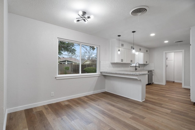 kitchen with a breakfast bar, white cabinetry, light hardwood / wood-style flooring, kitchen peninsula, and backsplash