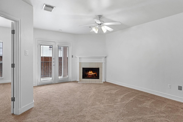 unfurnished living room with a tile fireplace, light colored carpet, and ceiling fan