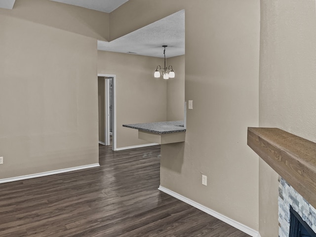 unfurnished dining area with dark hardwood / wood-style flooring, a stone fireplace, and an inviting chandelier