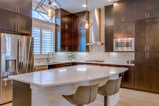 kitchen featuring a kitchen island, decorative light fixtures, sink, stainless steel appliances, and wall chimney range hood