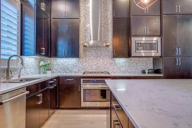 kitchen with sink, light stone counters, stainless steel appliances, dark brown cabinets, and wall chimney exhaust hood