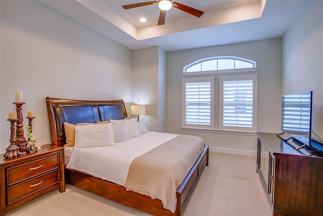 bedroom with a raised ceiling, light colored carpet, and ceiling fan