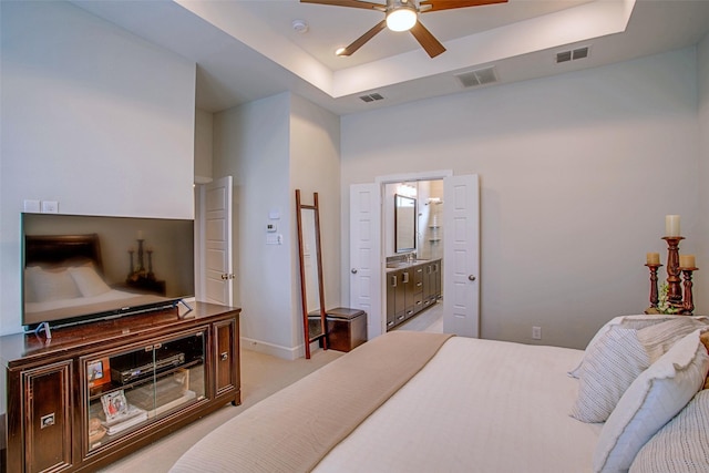 bedroom featuring a raised ceiling, connected bathroom, and light colored carpet