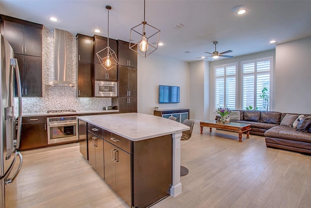 kitchen with hanging light fixtures, stainless steel appliances, a center island, light hardwood / wood-style floors, and wall chimney exhaust hood