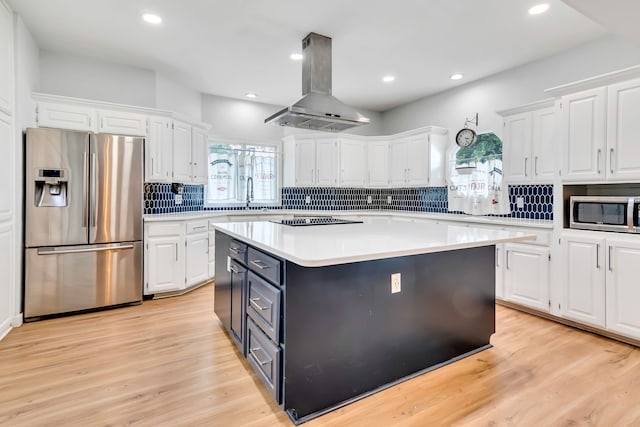 kitchen with appliances with stainless steel finishes, a kitchen island, white cabinetry, island exhaust hood, and light hardwood / wood-style flooring