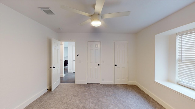 unfurnished bedroom featuring ceiling fan, light carpet, and two closets