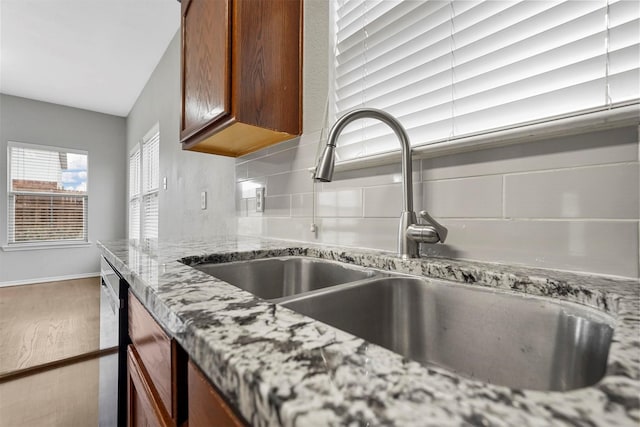 interior details with sink, stainless steel dishwasher, backsplash, and light stone counters