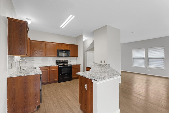 kitchen featuring sink, light hardwood / wood-style flooring, kitchen peninsula, light stone countertops, and black appliances